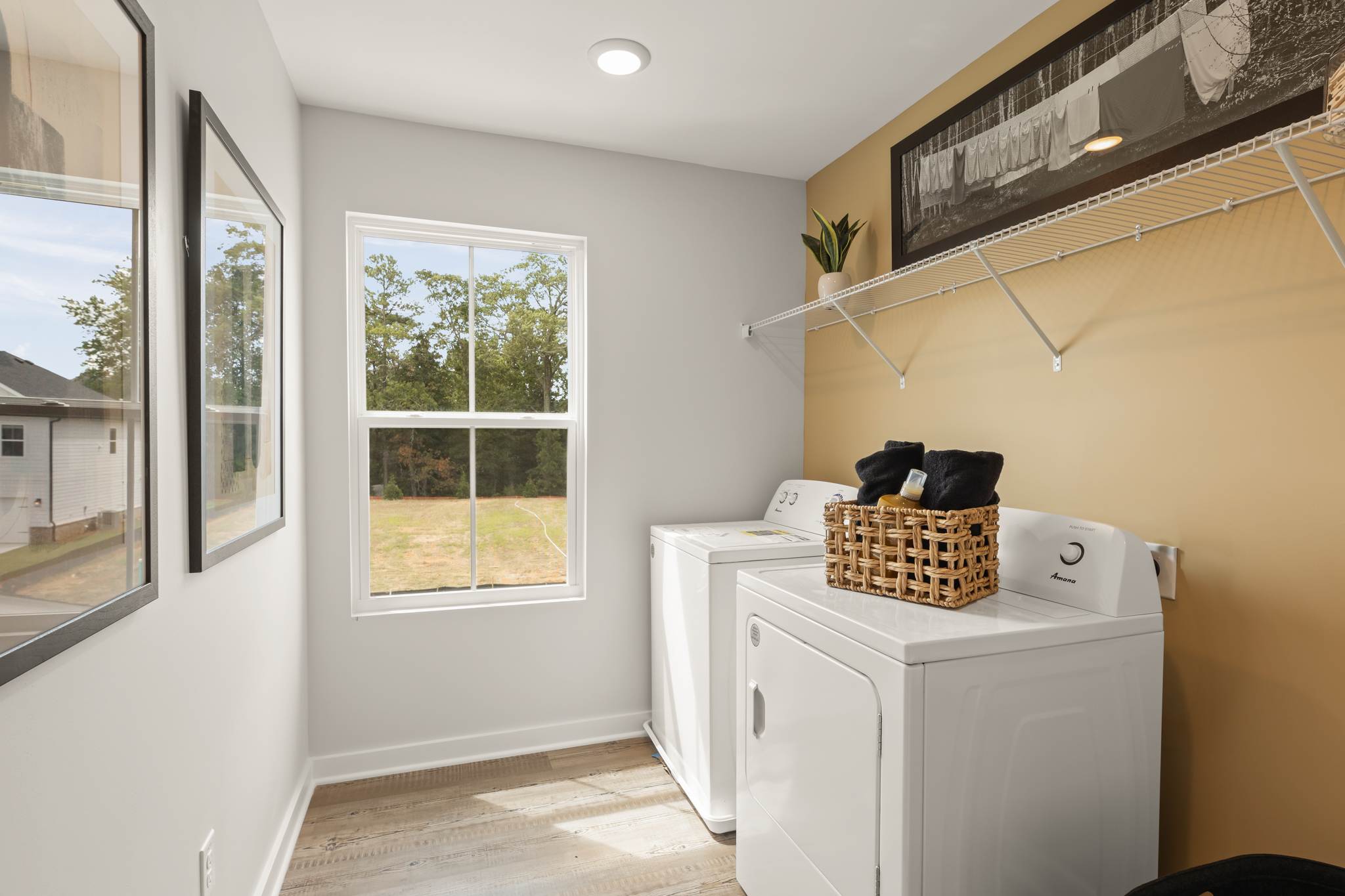 A room with a white laundry machine and a window with a basket on it.