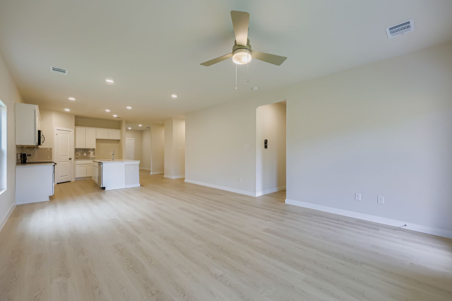 A large empty room with a ceiling fan and a wood floor.